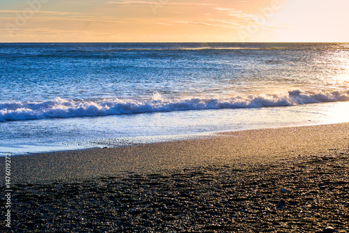 Golden sun light on black sand beach and ocean blue water on evening time in vik , Island.