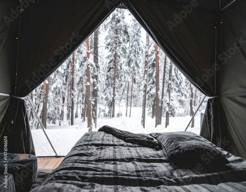 Cozy tent interior with view of snowy trees, creating serene atmosphere. dark tones of bedding complement winter landscape outside, inviting relaxation and warmth