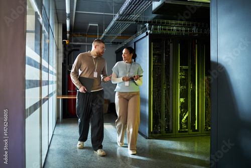 Wallpaper Mural Male and female colleagues engaged in conversation while walking through an IT server room with servers visible in background. He is holding tablet computer Torontodigital.ca