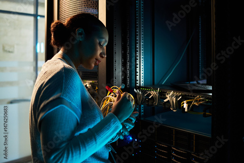 Asian woman inside a data center server room managing network cables and inspecting equipment, ensuring proper function and organization, surrounded by server racks