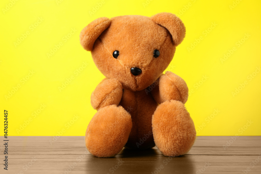 Fototapeta premium Cute teddy bear on wooden table against yellow background