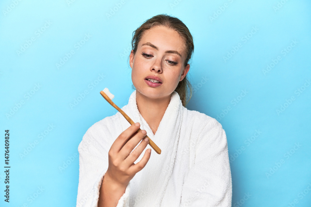 Young blonde woman in a robe holding a toothbrush in a studio Young blonde woman in a robe holding a toothbrush in a studio