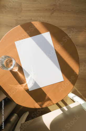 blank paper poster mockup on wooden coffee table with glass of water