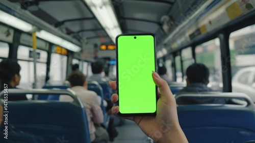 Wallpaper Mural A young woman holds a green screen phone on a bus, engaging with the smartphone for public communication. Her finger is seen touching the device as she scrolls through an application Torontodigital.ca
