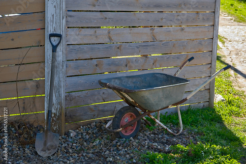 a wheelbarrow and a shovel by a wooden fence