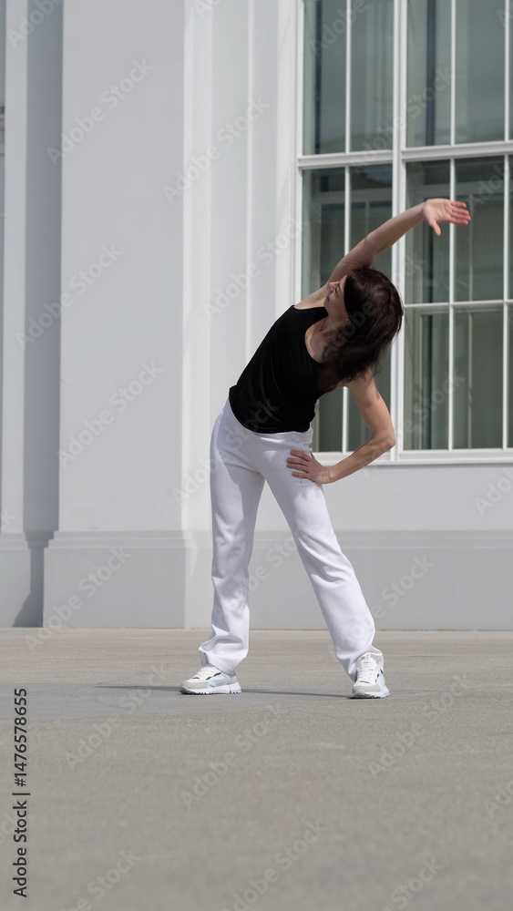 Naklejka premium A woman performs a side stretch outdoors, focusing on flexibility and body balance. This image represents wellness, mobility, and an active lifestyle.