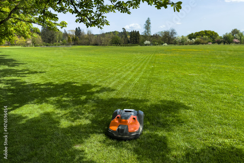 smart robotic lawn mower working at lush green meadow under tree shade. modern technology and eco-friendly gardening for sustainable