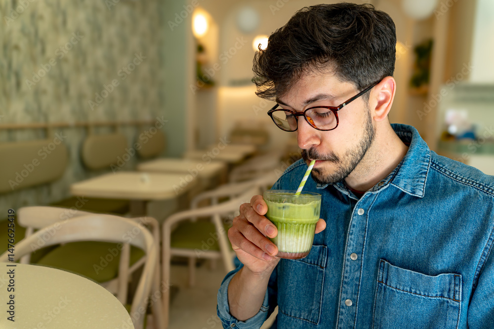 Fototapeta premium Customer enjoying a refreshing matcha latte in a modern cafe, savoring the vibrant green beverage