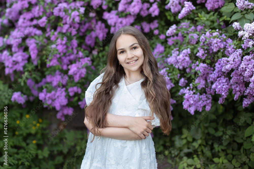 Fototapeta premium Portrait of a beautiful little girl in a lilac garden. A child girl walks in a flowered park. Outdoor fashion photo of a cute smiling young girl with long hair surrounded by flowers.
