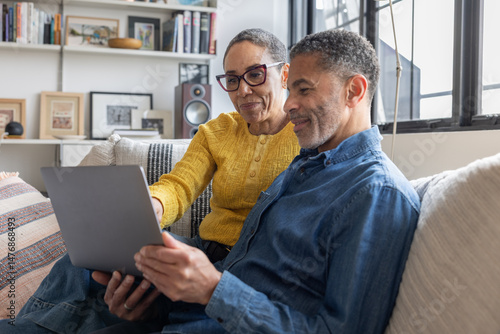 Mature couple relaxing at home on the couch using a laptop