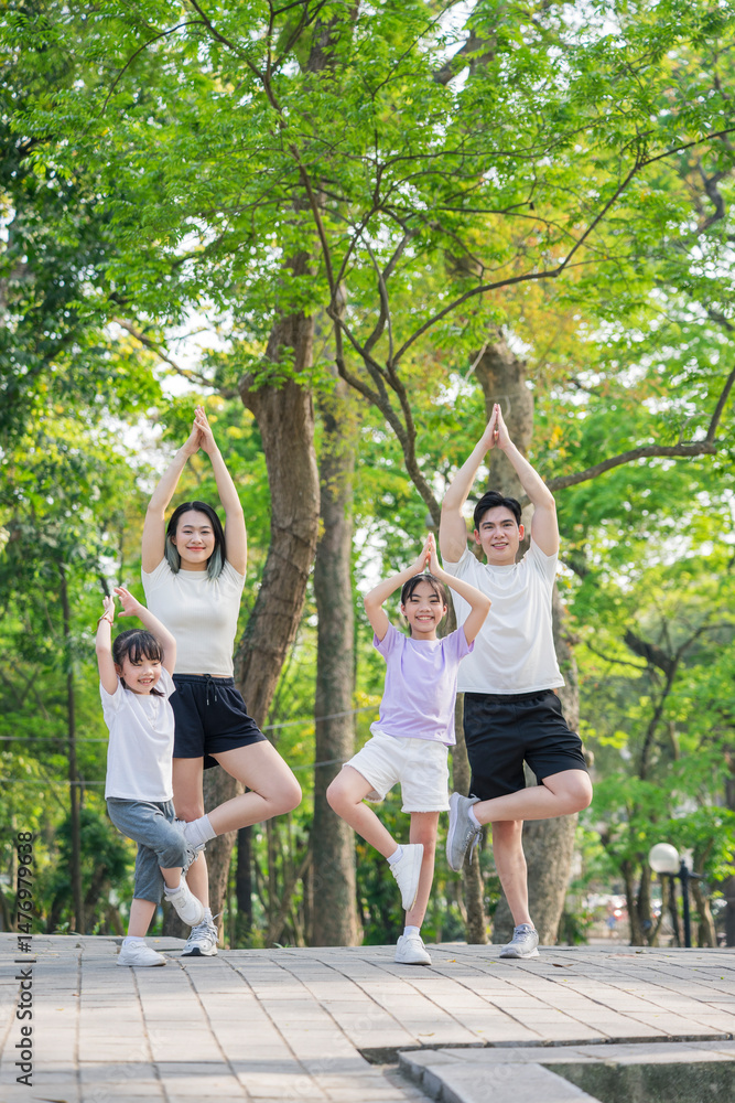 Fototapeta premium Family practicing yoga poses together in a green park during a sunny day