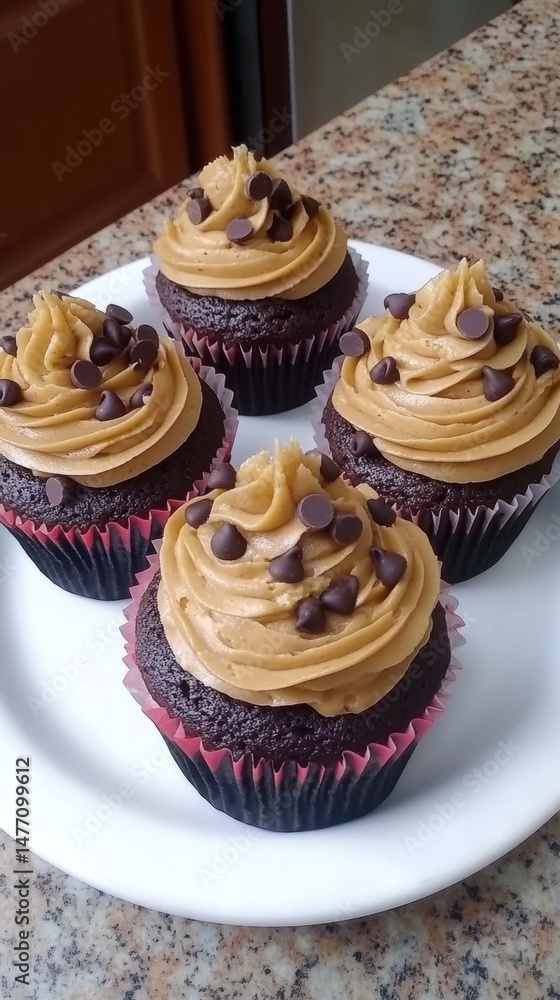 Four chocolate cupcakes with peanut butter frosting and chocolate chips on a white plate close up studio shot Four chocolate cupcakes with peanut butter frosting and chocolate chips on a white plate close up studio shot
