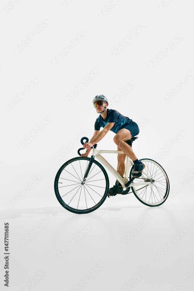 Obraz premium Side view low angle image of focused man, professional cyclist in full gear, riding bike, training isolated on white background. Concept of sport, competition, active lifestyle, endurance