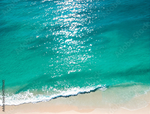 Summer beach background. Crystal clear tropical ocean water. Calm waves and glimmering sunshine. Drone view. 
