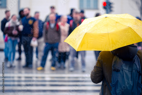 Yellow umbrella against defocused people staying on a crosswalk in the rain