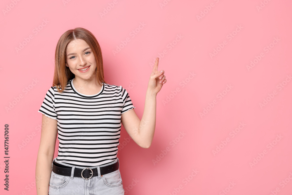Portrait of smiling teenage girl pointing at something on pink background. Space for text Portrait of smiling teenage girl pointing at something on pink background. Space for text