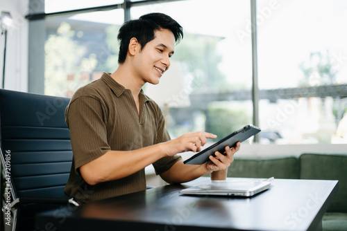 young man working on laptop at bright modern office desk with coffee and tablet. Ideal for tech, freelance, business, and remote work themes. Free Download young man working on laptop at bright modern office desk with coffee and tablet. Ideal for tech, freelance, business, and remote work themes. - GFXLoad