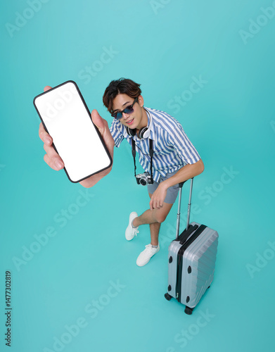 Top view Happy smiling young asian man tourist in summer clothes and baggage showing mockup mobile cell phone app booking hotel isolated on blue background.