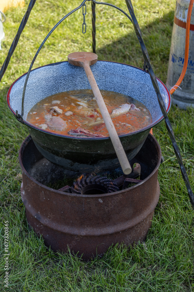 Traditional Hungarian fish soup simmering in a cauldron over open fire Traditional Hungarian fish soup simmering in a cauldron over open fire