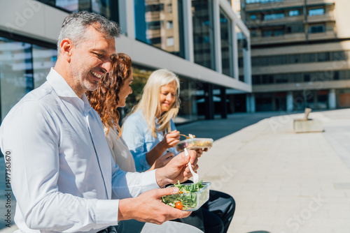 Obraz na plátně Business professionals sharing midday meal outdoors, sitting on bench near corpo