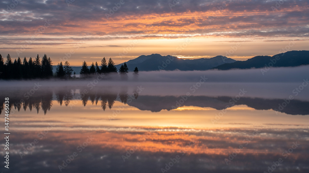 Fototapeta premium Tranquil Lake Reflection at Sunrise with Mist and Mountains in the Distance