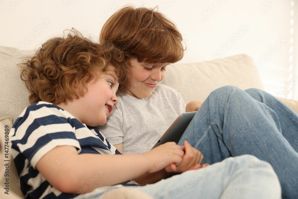 Cute little brothers with tablet on sofa at home Cute little brothers with tablet on sofa at home
