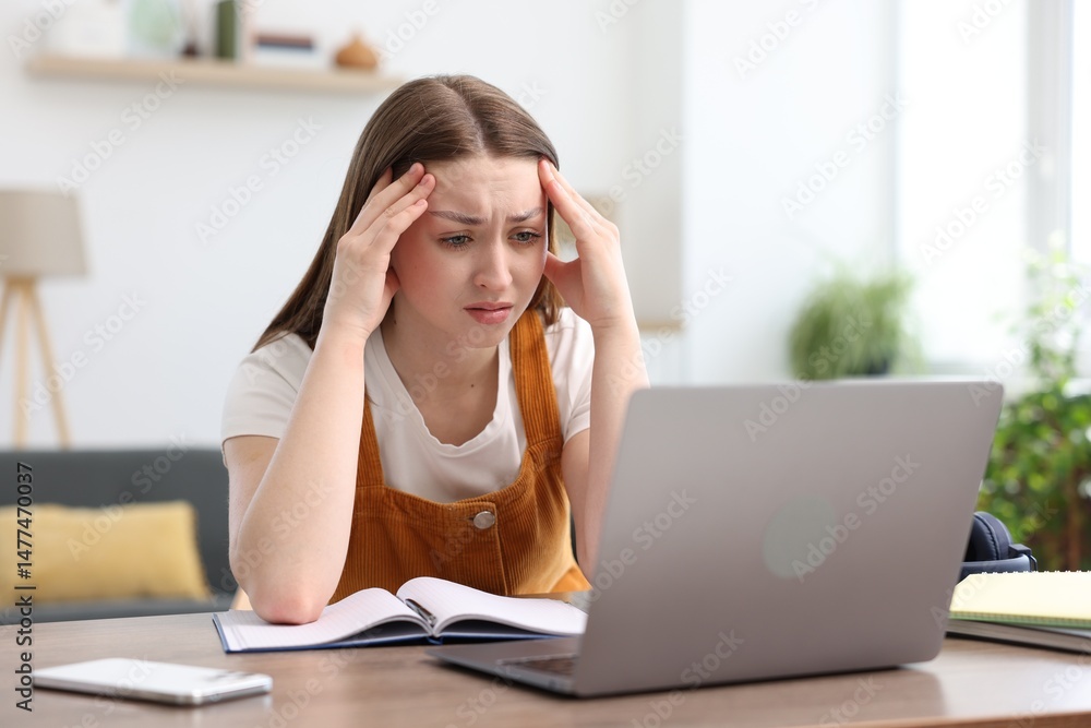 Teenage girl doing homework with laptop at table indoors Teenage girl doing homework with laptop at table indoors