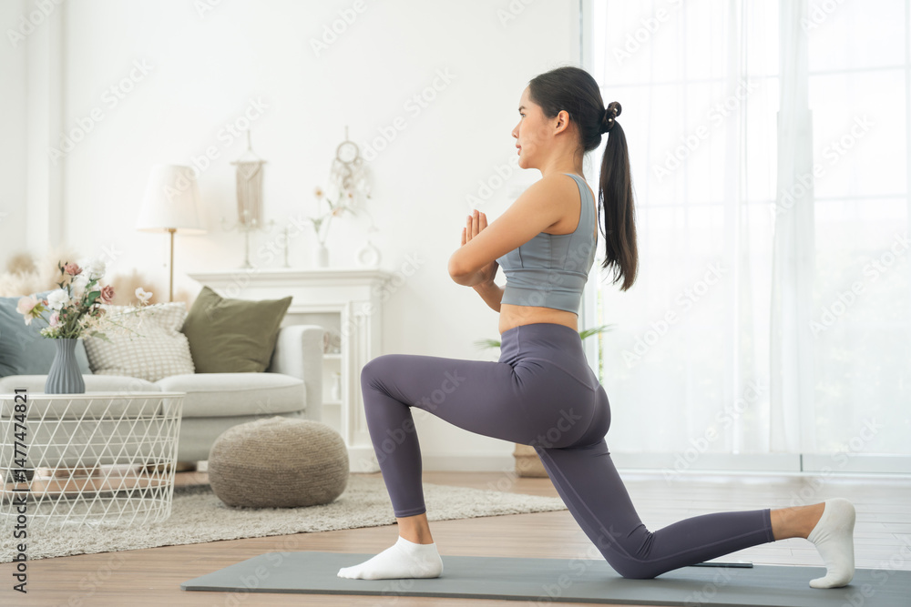Fototapeta premium Young Asian woman in sportswear doing yoga in her home or house for health, sports and wellness, Enjoying Domestic Fitness Training And Healthy Lifestyle, Dressed In Stylish Sportswear And Smiling