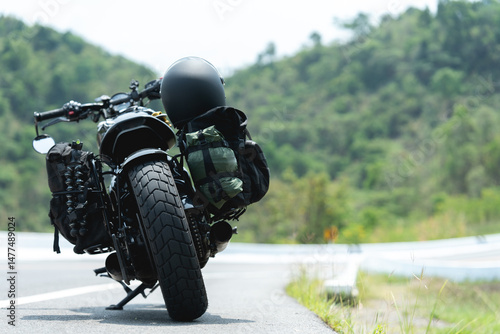 A motorcycle with gear is parked on a scenic winding road, surrounded by green hills and trees.