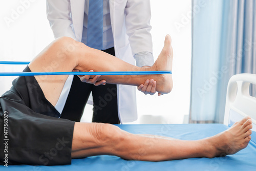 An elderly patient undergoes leg physiotherapy on a treatment bed while being carefully assisted and advised by a healthcare specialist.