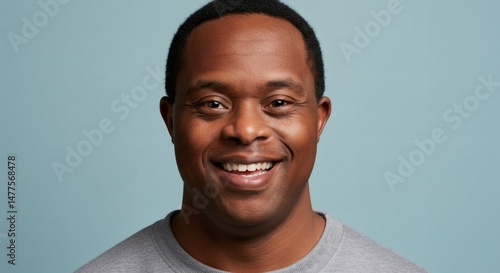 A friendly portrait of a man with Down syndrome, smiling brightly against a blue backdrop.