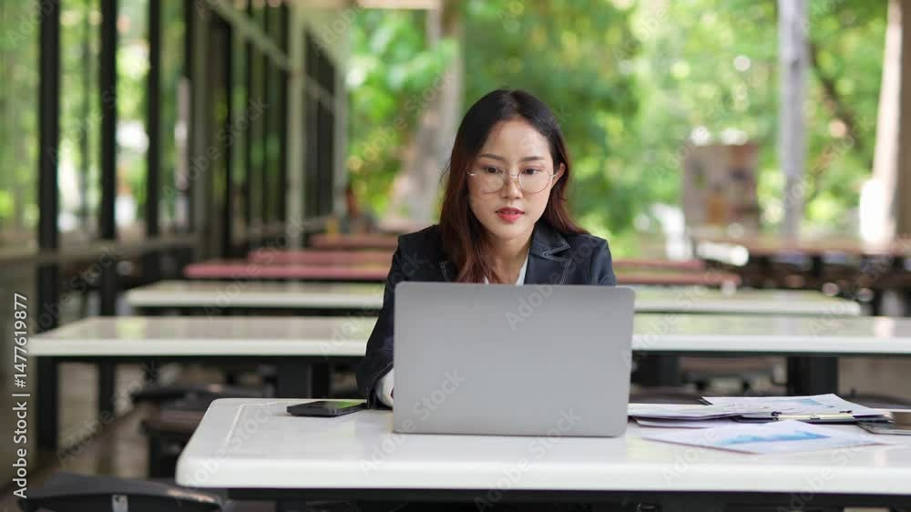 Asian businesswoman working at desk using laptop and notebook talking to client or office building, slow motion footage Asian businesswoman working at desk using laptop and notebook talking to client or office building, slow motion footage