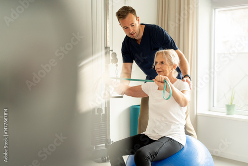 Obraz na plátne Senior woman working out with resistance band under the guidance of a physiother