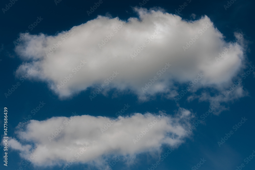 Fototapeta premium A pair of soft, white cumulus clouds float in a rich blue sky, creating a peaceful and minimal composition with ample copy space.