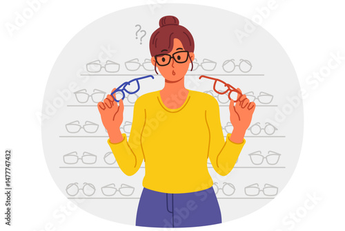 Woman buys glasses in store with large assortment of lenses and frames and chooses one of two options. Girl stands near display case with glasses in ophthalmic shop, allowing to solve vision problems.