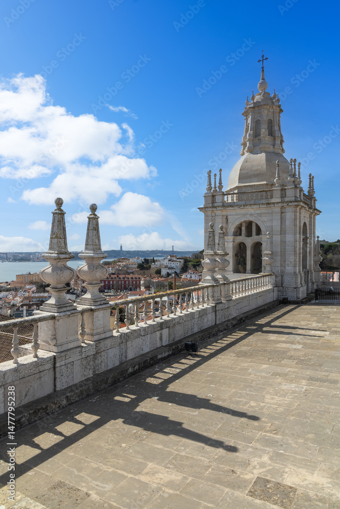 Obraz premium Rooftop view of the historic São Vicente de Fora Monastery in Lisbon, overlooking the Tagus River and cityscape under a bright sky.