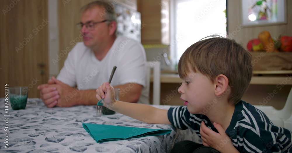 Boy sitting at table with family nearby, engaged in quiet and natural interaction, authentic glimpse into daily family routine in a warm kitchen setting Boy sitting at table with family nearby, engaged in quiet and natural interaction, authentic glimpse into daily family routine in a warm kitchen setting