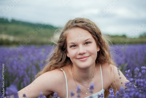 Portrait of happy girl near lavender. Curly model 13 years old with long hair in field of purple flowers. Summer.