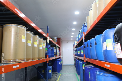 Pharmaceutical warehouse with blue storage containers on racks, clean epoxy flooring, cleanroom environment in supplement or medicine manufacturing facility.