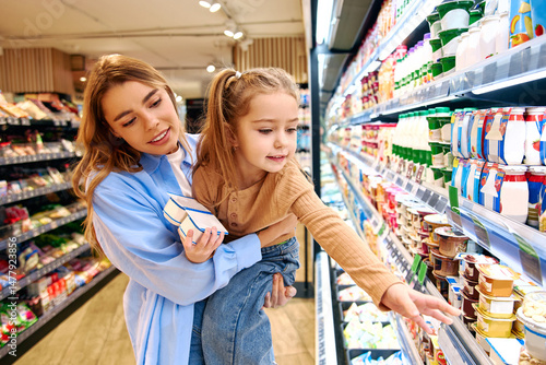 Принти на полотні Mother and daughter choosing dairy products together in supermarket refrigerator