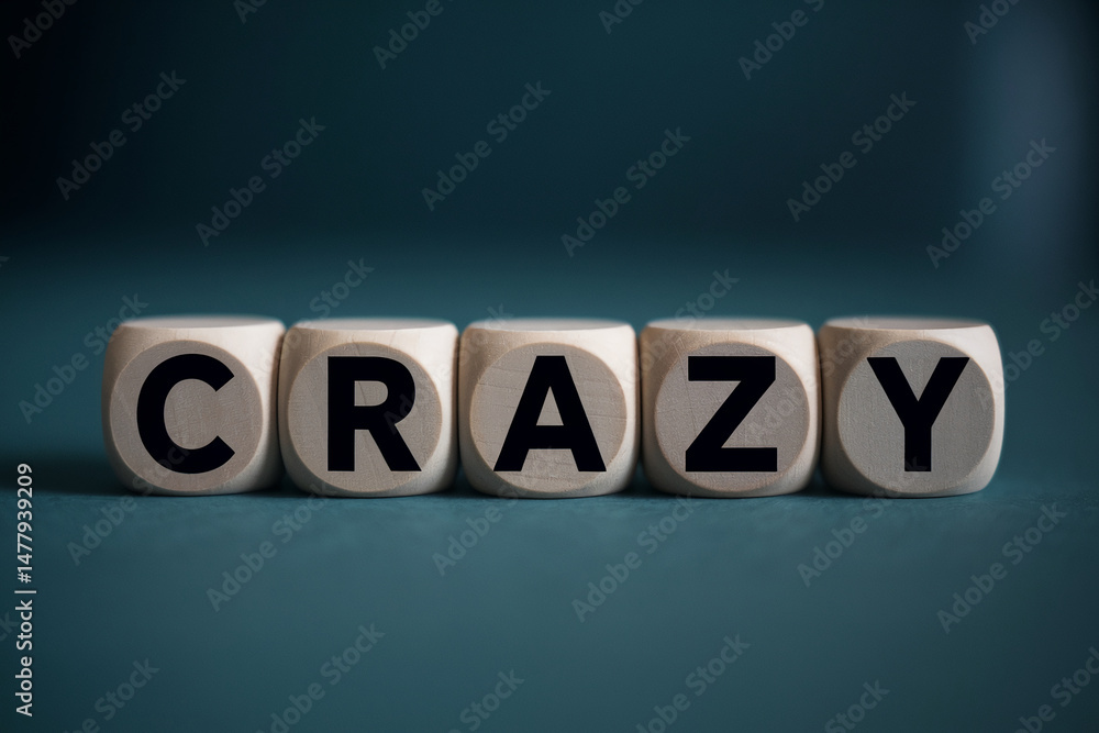 Obraz premium Wooden cubes spelling word crazy on teal background, showcasing concept of unconventionality and spontaneity