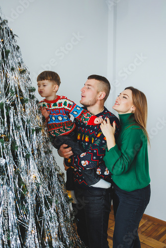 Obraz na płótnie A joyful family celebrates the holiday season in their cozy home, enjoying laughter and love around a beautifully decorated Christmas tree filled with colorful decorations and thoughtful gifts w salonie