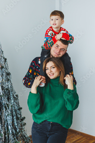 Obraz na płótnie A heartwarming family portrait showcasing a joyful child happily posed in cheerful Christmas sweaters beside a beautifully sparkling holiday tree, capturing the true essence of the joyful season w salonie