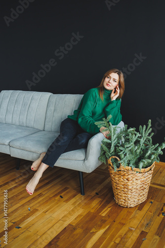 Obraz na płótnie In this casual home living scene, a stylish woman enjoys moments of relaxation on a modern sofa adorned with beautiful indoor plants that add a touch of greenery and elegance to her home w salonie