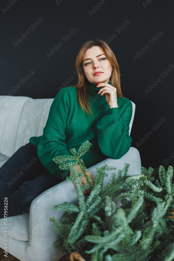 An elegant woman gracefully wearing a green sweater is striking a pose on a cozy sofa, surrounded by a variety of lush indoor plants, creating a vibrant atmosphere infused with life and style