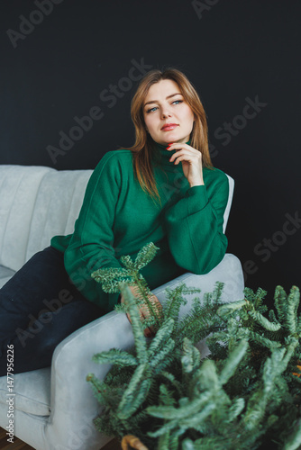 Obraz na płótnie An elegant woman gracefully wearing a green sweater is striking a pose on a cozy sofa, surrounded by a variety of lush indoor plants, creating a vibrant atmosphere infused with life and style w salonie