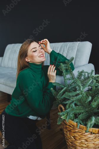 A joyful woman wearing a soft green sweater joyfully poses gracefully alongside a vibrant indoor plant in a cozy, warm living room, which creates a truly welcoming atmosphere for all who enter
