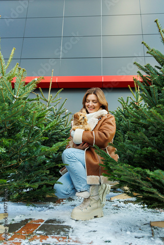 Obraz na płótnie Charming Winter Moment A Young Woman Holding a Cute Dog, Surrounded by Beautiful Christmas Trees, Creating a Wonderful Atmosphere Full of Joy and Celebration in the Festive Season w salonie