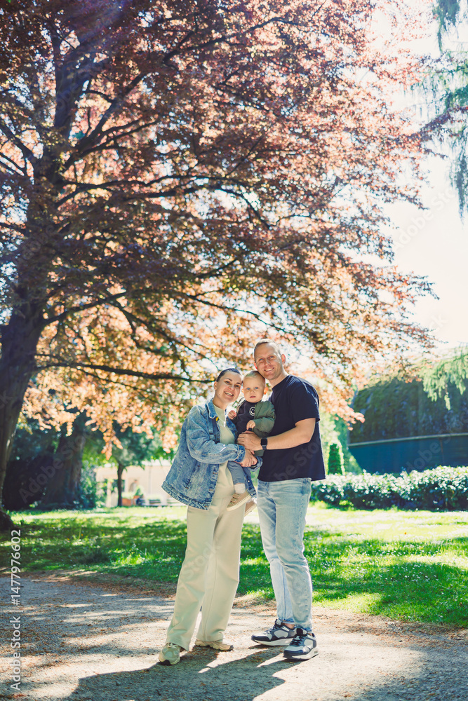 A heartwarming family portrait set against a majestic tree in a sunlit park surrounded by vibrant colorful foliage that highlights the beauty of autumn, showcasing the joy and love within the family