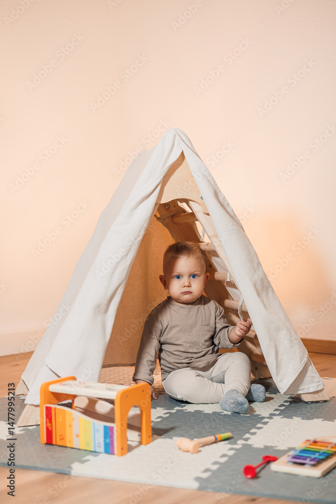 A happy baby sits in a cozy play tent, surrounded by colorful toys on the floor, creating a delightful setting for joyful memories and imaginative play, fostering creativity and joy in childhood